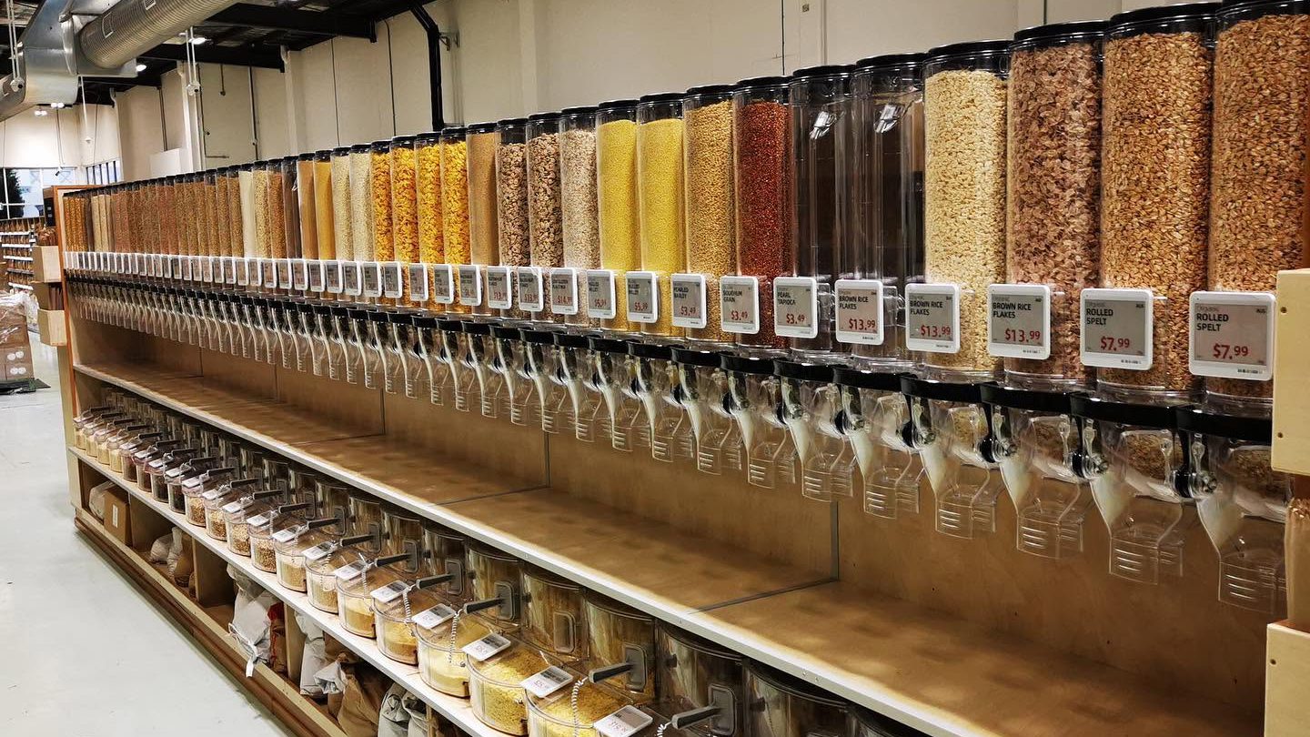 The bulk wall — a long row of gravity dispensers of organic grains, flakes and cereals with price tags on every canister, and tubs and paper sacks of loose goods on the shelves below.